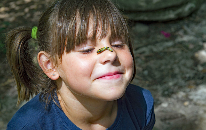 A caterpillar crawls over the bridge of a young girl's nose