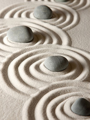 four gray stones are arranged in sand with each having concentric ripples of sand emanating out from them