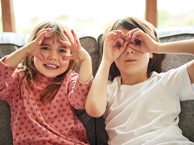 two children on sofa holding fingers over eyes