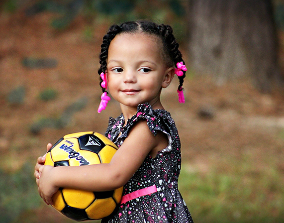 child smiling holding soccer ball in arms
