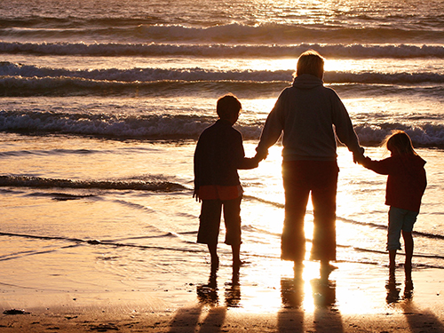 adult holding hands with two children on beach at sunset
