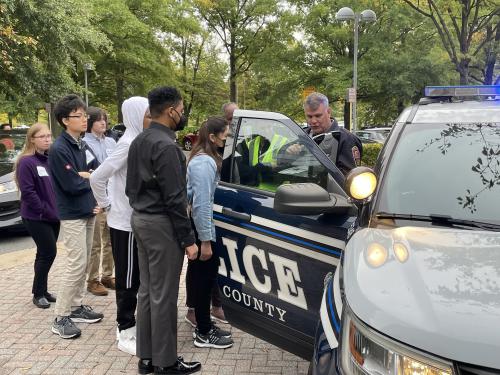 Students stand next to police car and learn about law enforcement. 