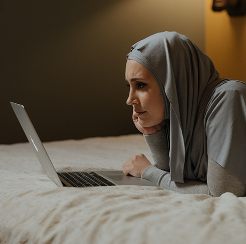 woman laying on bed looking at laptop