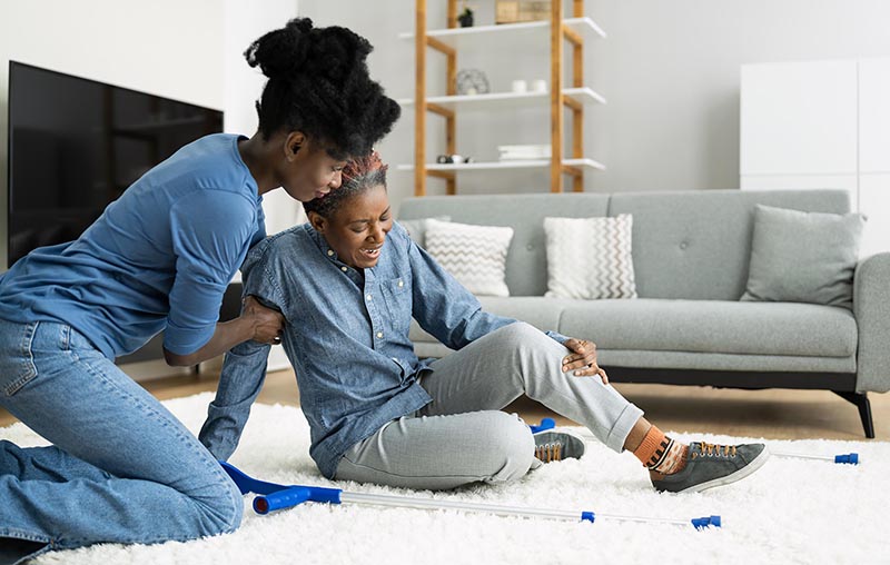 Photo of a younger woman helping an older woman who has fallen in a living room
