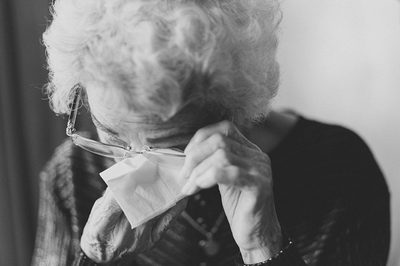 Photo of an older woman wiping her eye with a tissue