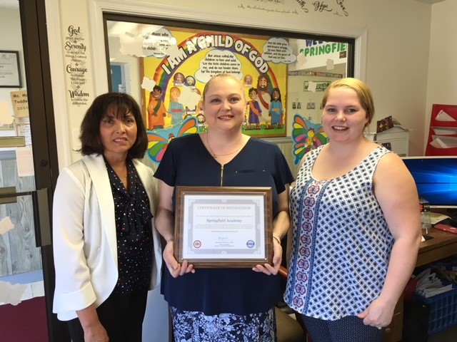 Springfield Academy Director Jennifer Schwitz and Administrative Support Professional Angela Todd accept a certificate of recognition from Christine Carlock with the Fairfax County Health Department. 