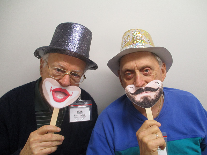 Two male ADHC participants wear a hat and smiley mouth mask for World Smile Day