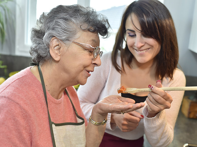 Daughter offers elderly mother soup to taste on a spoon