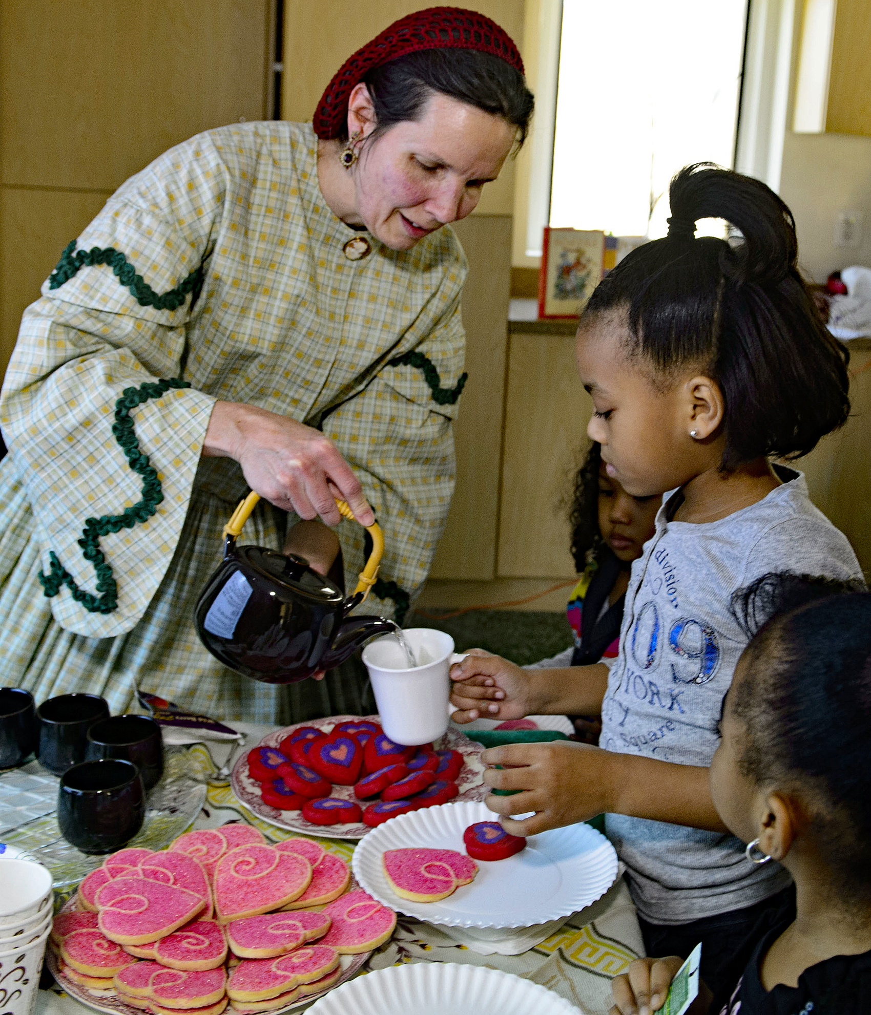 Docent in costume pours tea for a young child
