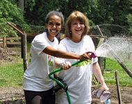 Two ECLP volunteers play with a water hose while working in a garden