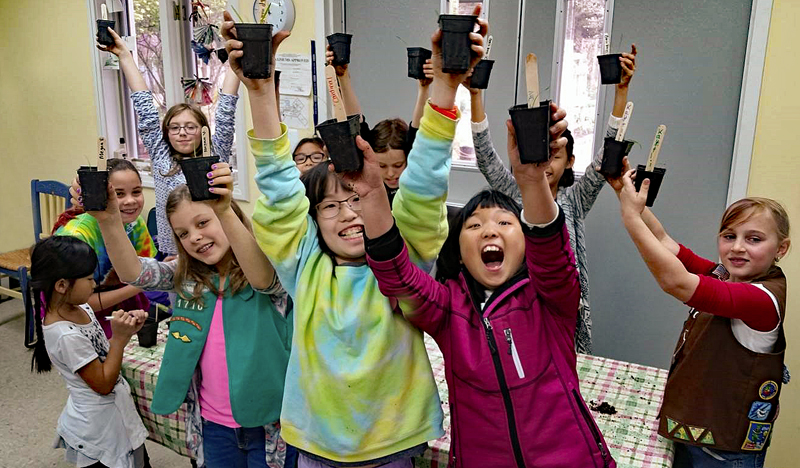 A troop of Girl Scouts raise high pots with seeds they have planted