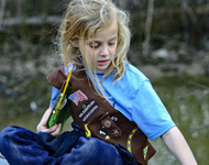 Young Brownie scout sits on boardwalk and points at a natural resource
