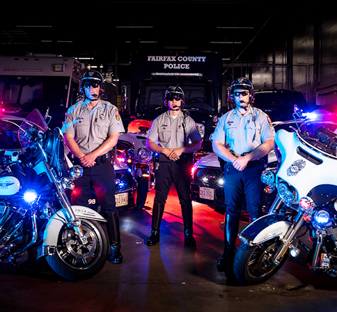 motorcyle officers pose in front of Fairfax County Police Department vehicles