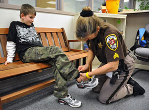Sheriff's deputy changes transmitter battery in boy's ankle band.