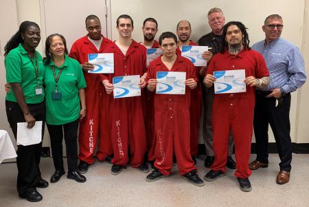 Six inmates hold their ServSafe certificates with Aramark and Sheriff's Office staff