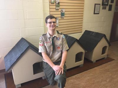 Boy Scout sitting in front of cat houses