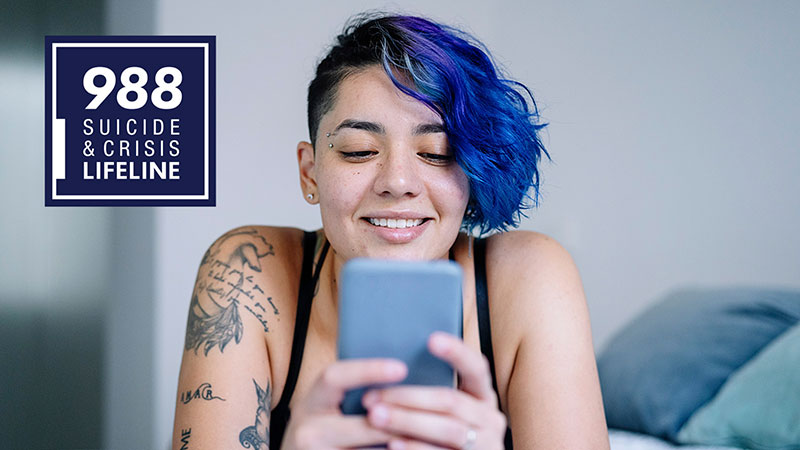 A person types into their smartphone with the logo of the 988 Suicide and Crisis Lifeline placed in the corner of the photo.