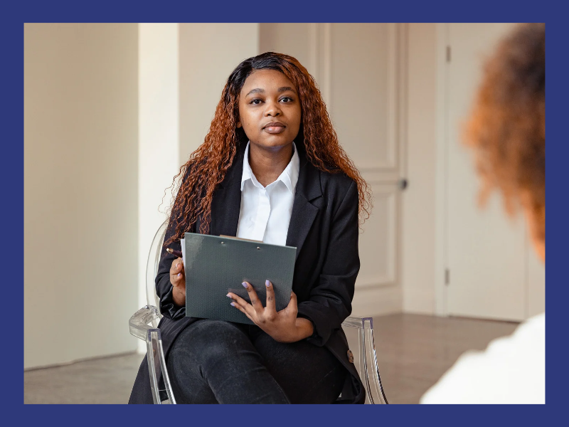 A clinician holding a clipboard sits listening to a client