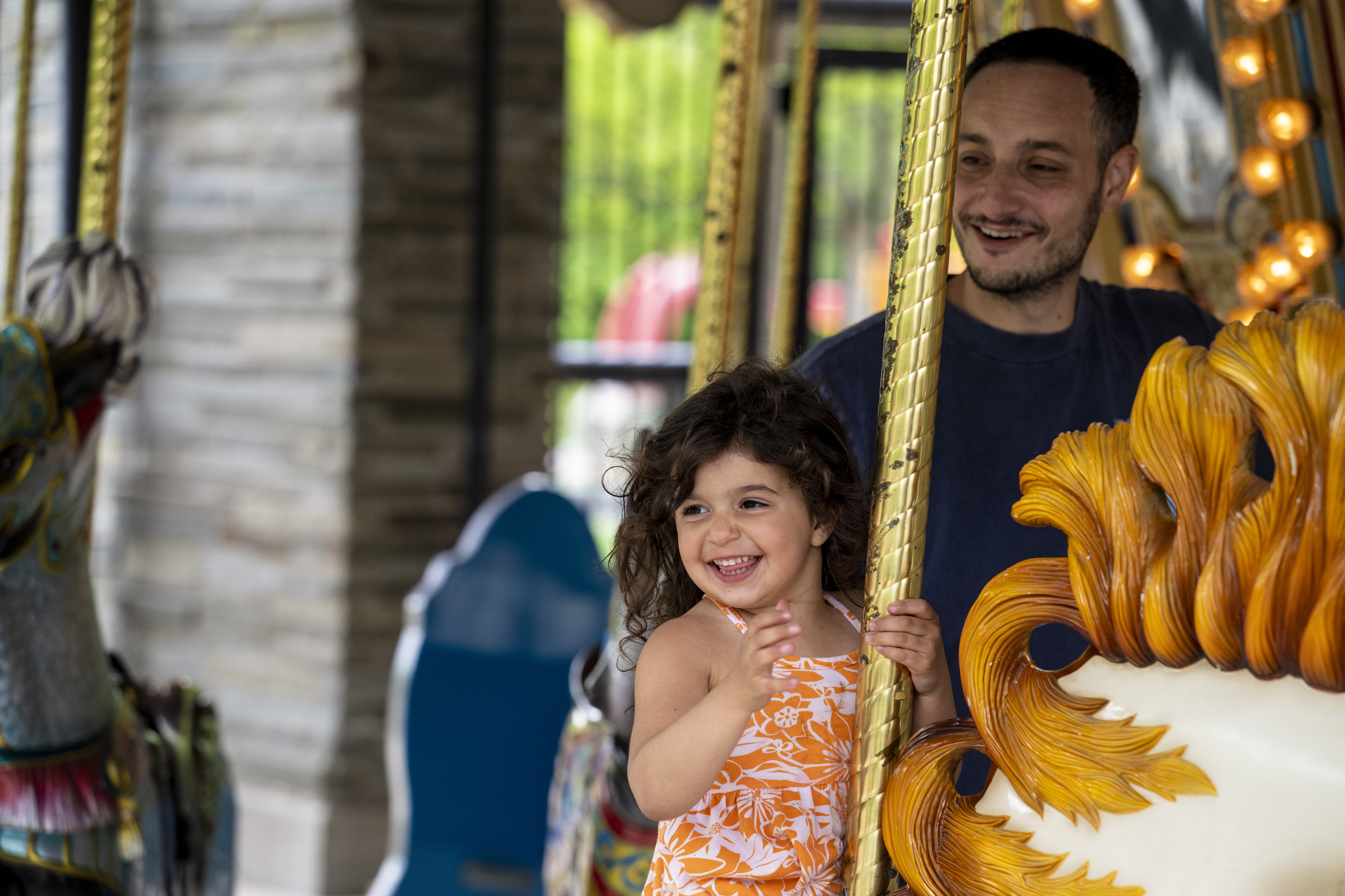 A young girl rides the carousel and her father stands behind her