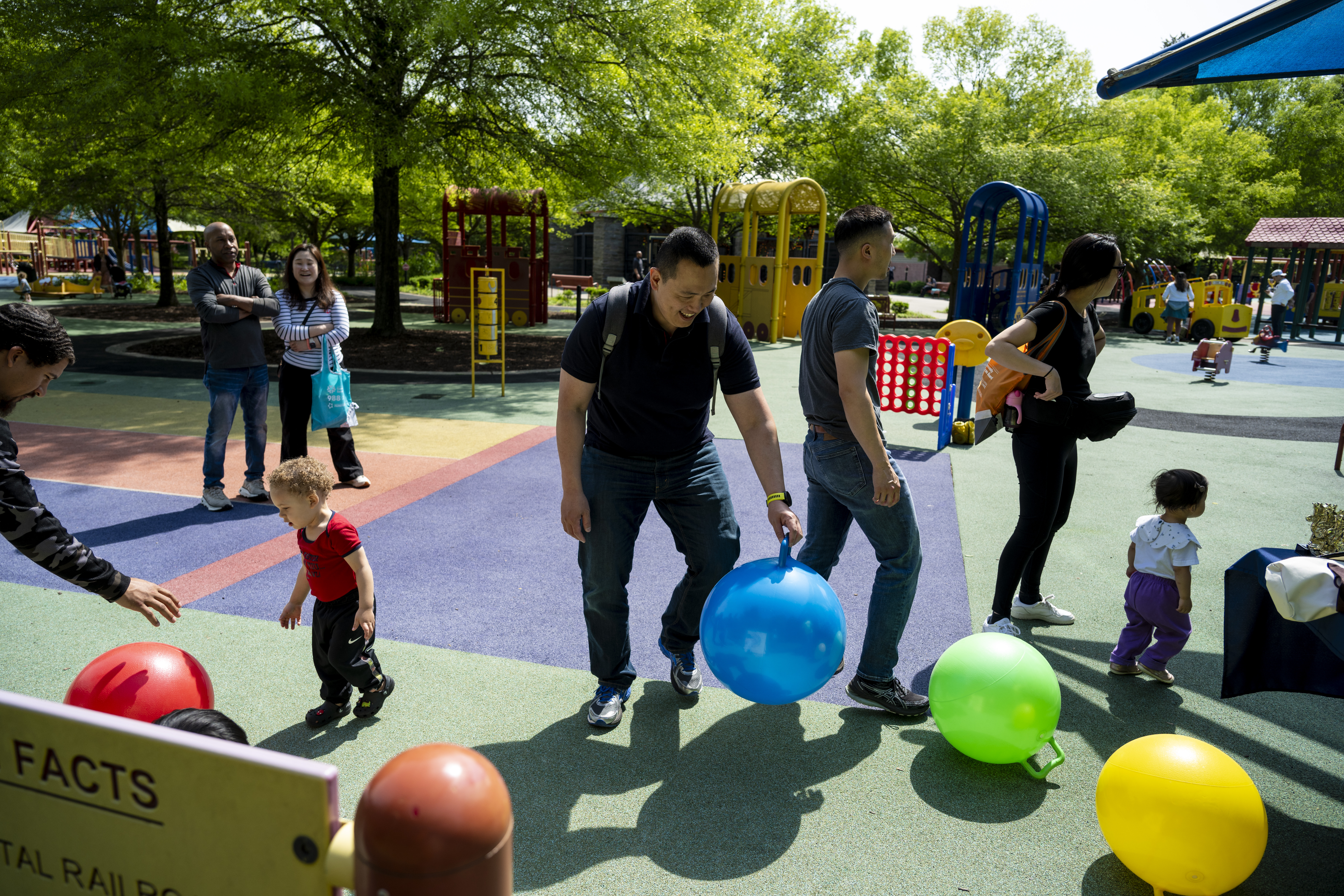 Several adults and children walk around and play with colorful balls at Clemyjontri Park