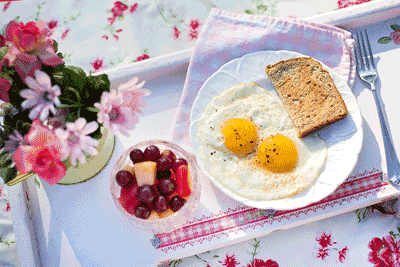 Photo of breakfast tray with flowers, fruit, eggs and toast.