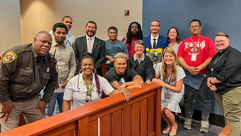 A group of adults, some of the sheriffs and one in judicial robes, pose together in a courtroom.