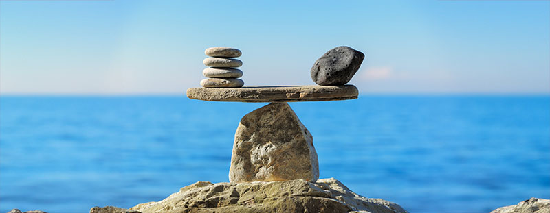 A rock cairn int the style of the scales of justice with rocks balanced at the ends of a flat rock resting single point.
