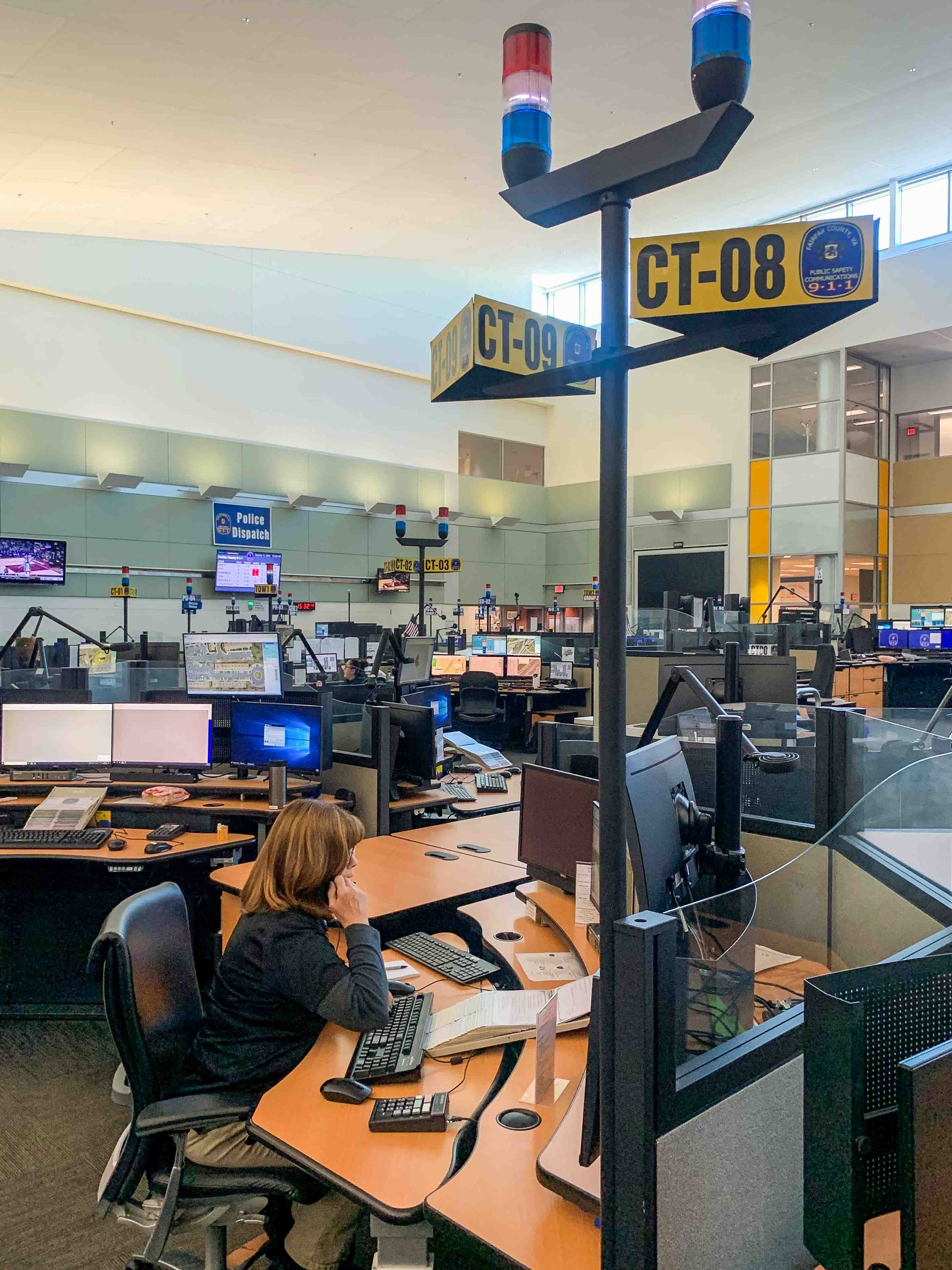 woman sitting at desk at 9-1-1 call center speaking on phone and working on a computer