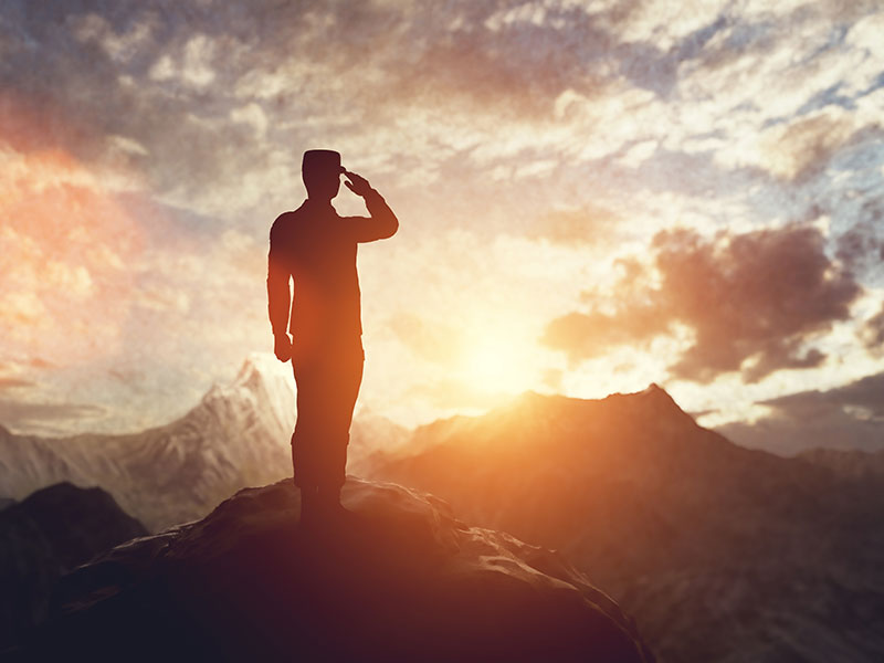 the silhouette of a soldier standing on a rocky hill and saluting