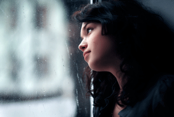 Photo of teen girl looking out rainy window