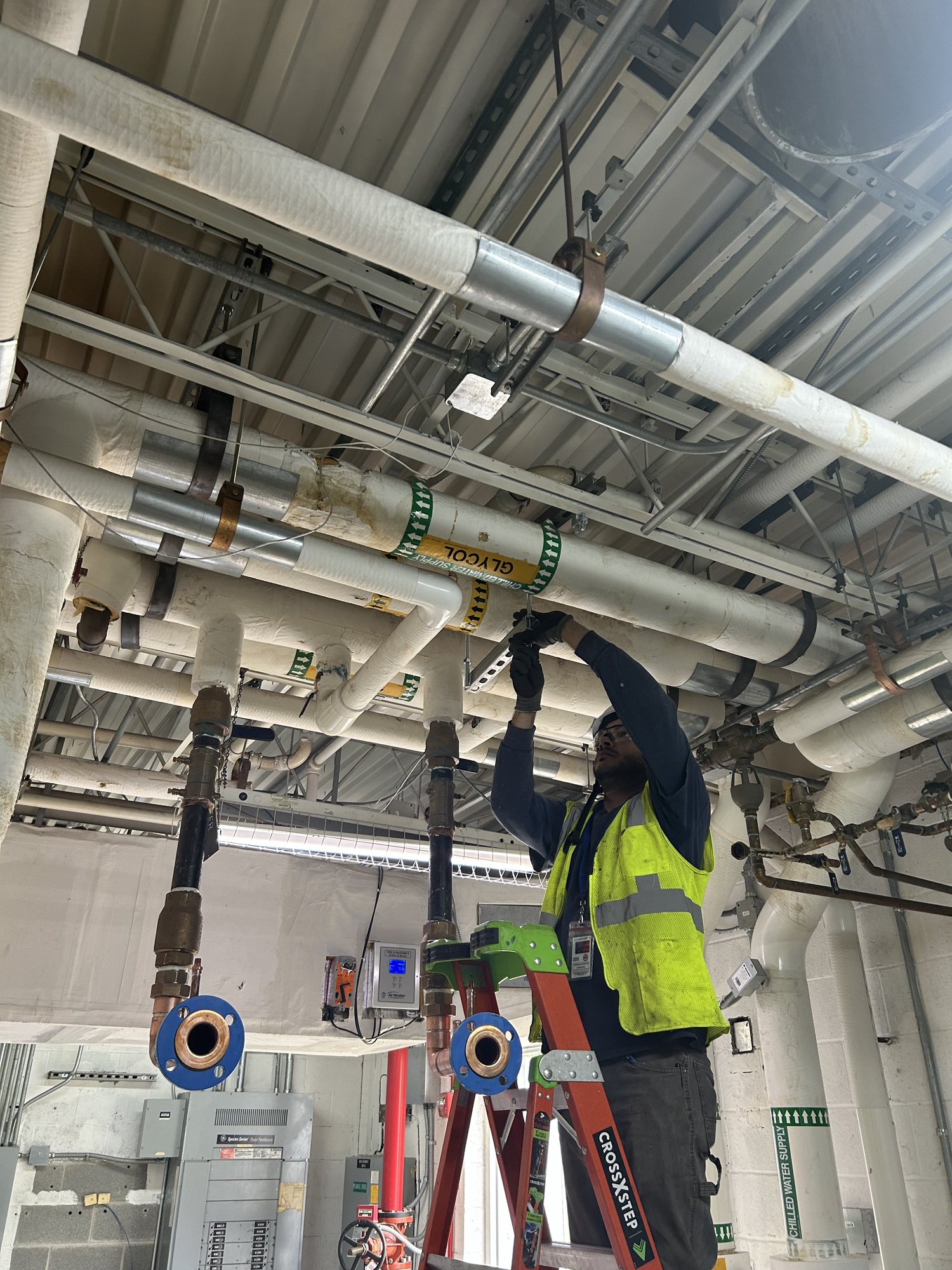 worker on ladder fixing a large silver pipe