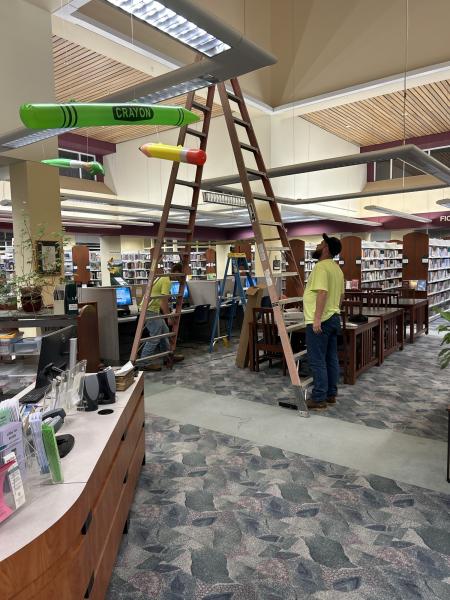 photo of man looking at lighting on ceiling with a ladder in a library