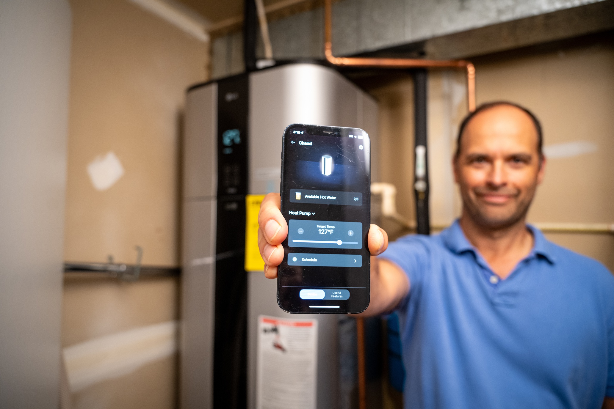 photo of a man holding up a phone showing energy efficiency numbers from a heat pump