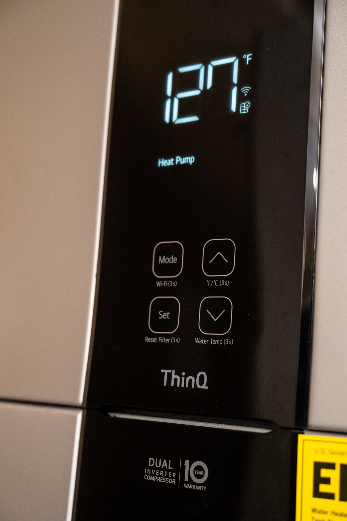 Close-up of a smart heat pump display showing 127°F with control buttons and branding.