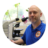 headshot of man wearing blue shirt in front of a microscope