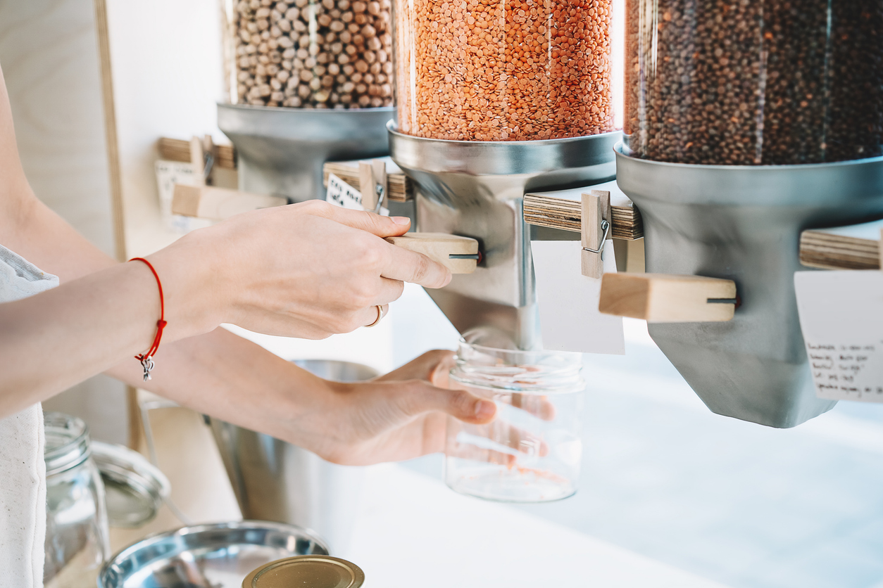 Close-up image of woman pours red lentils in glass jar from dispensers in plastic free grocery store