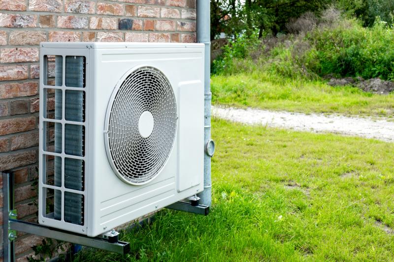 Outdoor air conditioning unit mounted on a brick wall surrounded by grass.
