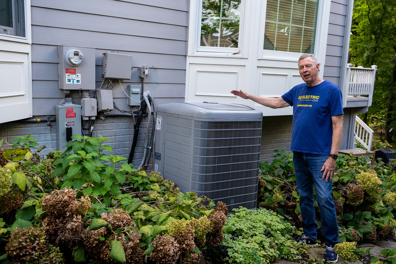 A person standing beside an outdoor HVAC unit attached to the side of a house.