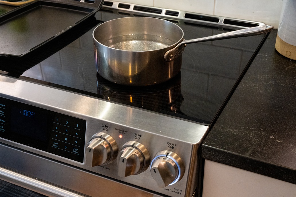 A pot of water heating on a glass-top electric stove with control knobs visible.