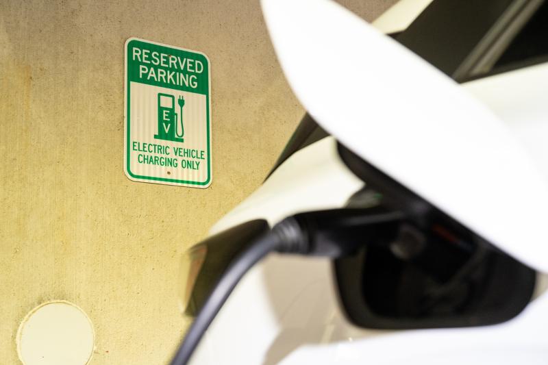 White electric car plugged in at a reserved EV charging parking spot.