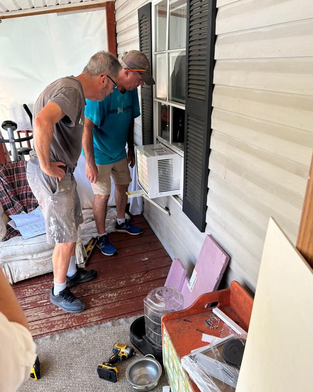 two men looking at a AC unit on the outside of a home