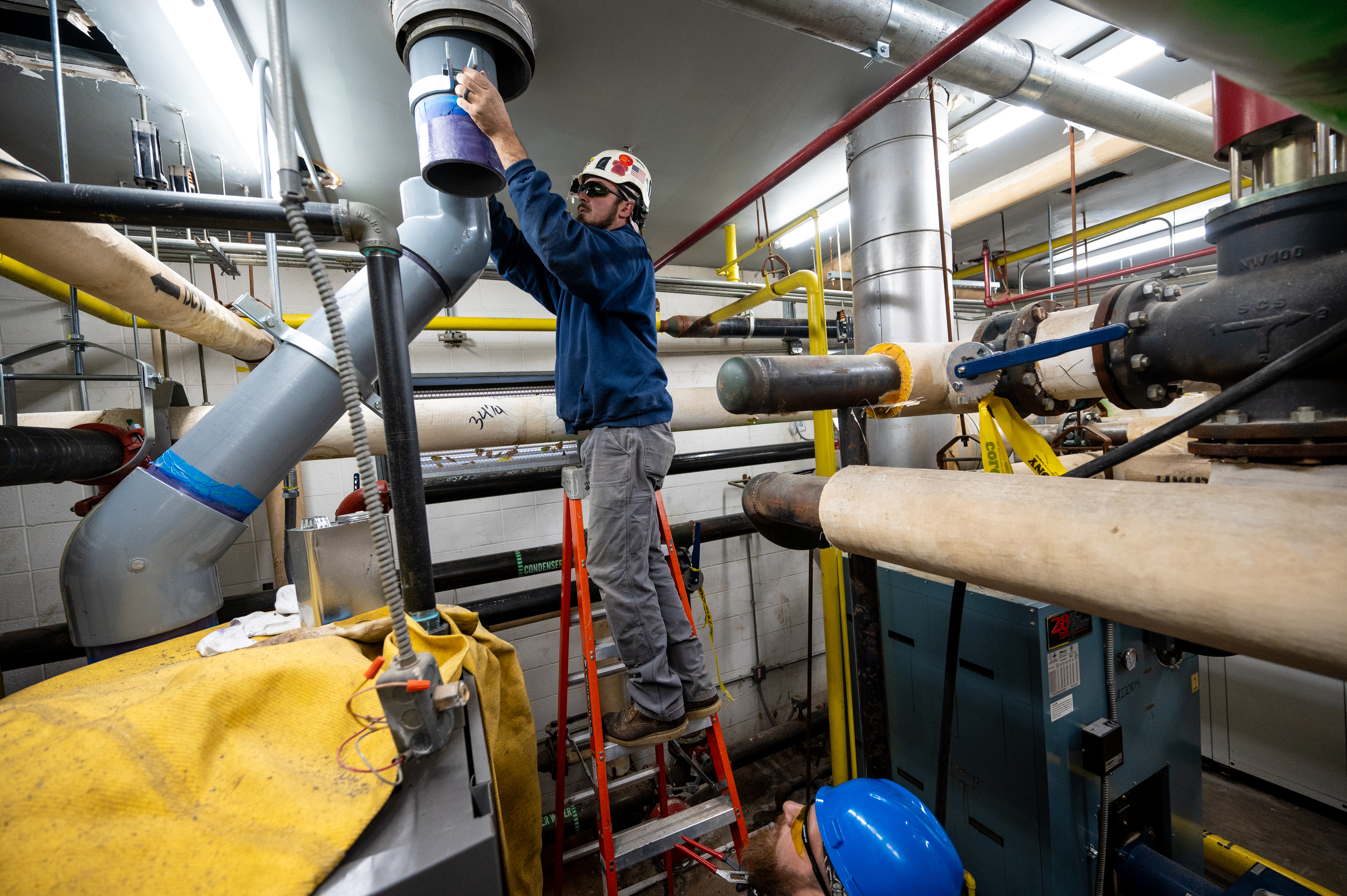 two workers installing PVD piping in a ceiling