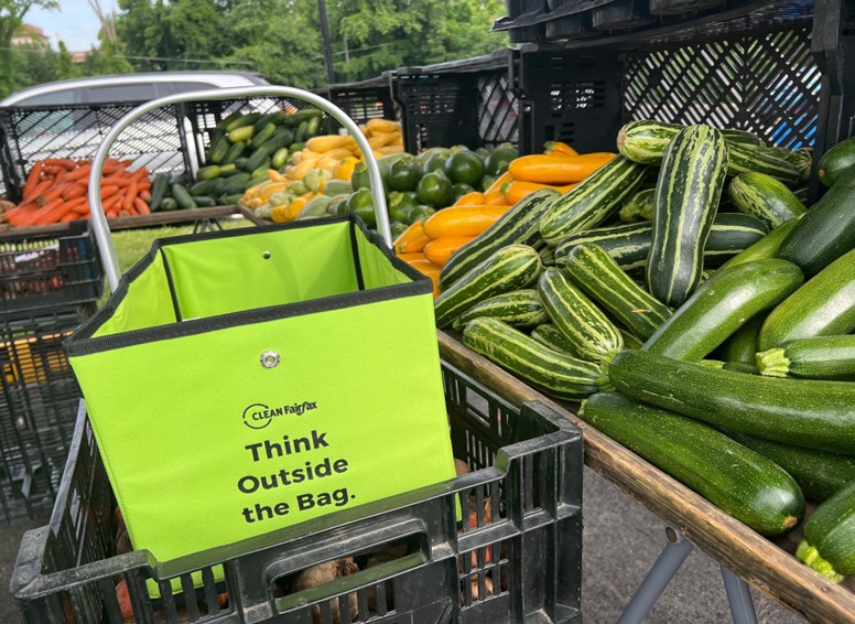 a bright green bag with Clean Fairfax logo and the words "Think Outside the Bag" pictured at a farmers market