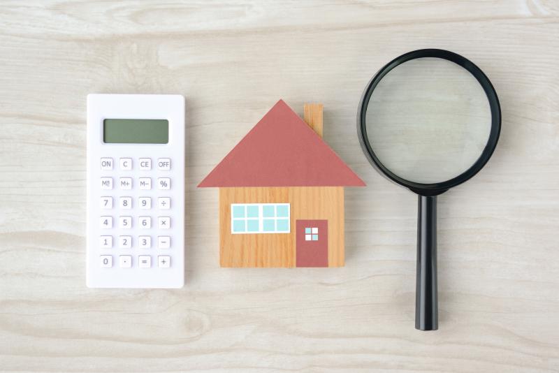 House object and magnifying glass with calculator on natural wooden table