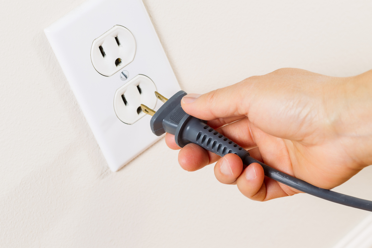 Horizontal photo of female hand removing power cord receptacle into electric wall outlet