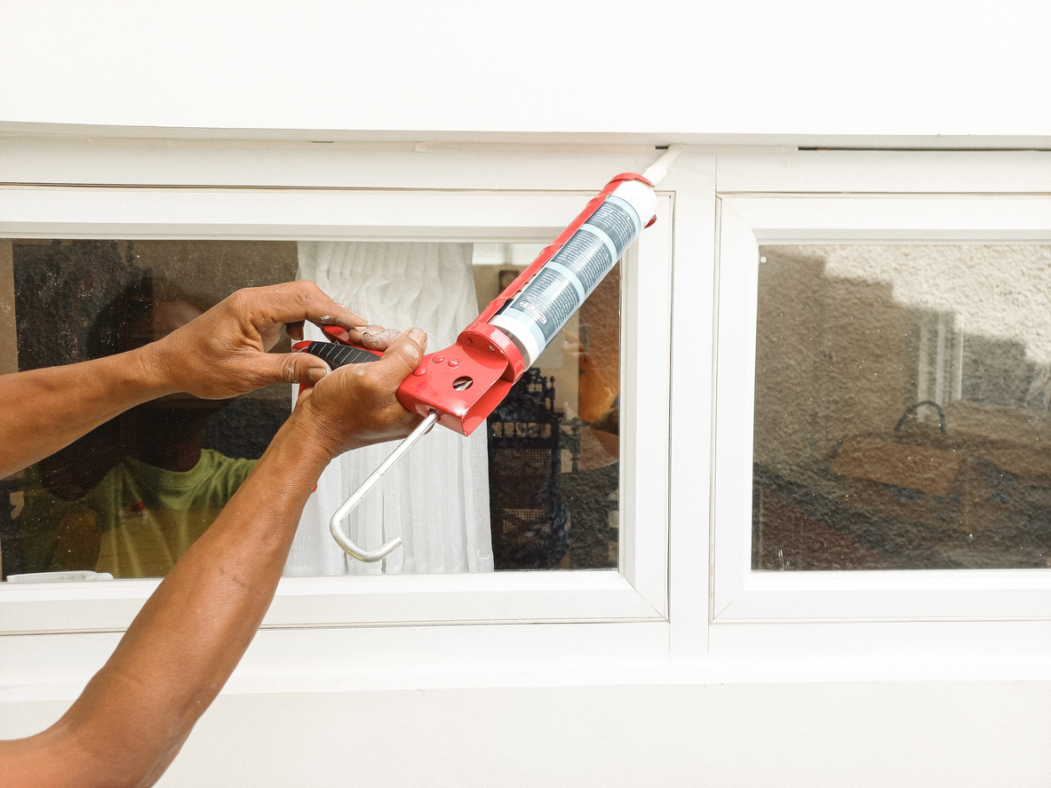 Hands Applying Weather Seal Caulk to Window Frame.