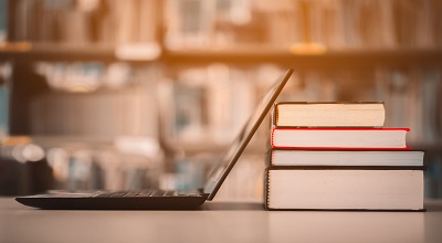 An image of a laptop with a pile of books