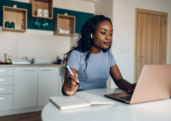 woman sitting at desk with a notebook and laptop, taking notes