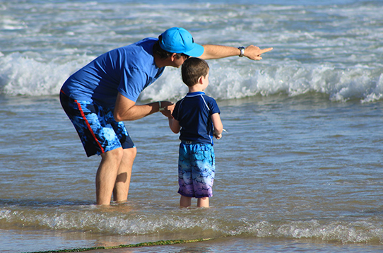 adult standing with child in water