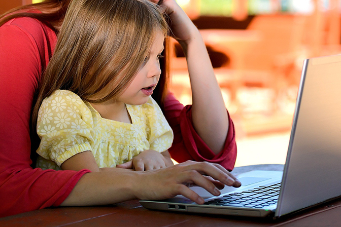 child sitting with adult using laptop